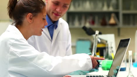 Science-students-examining-chemical-and-using-laptop