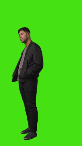 vertical video full length shot of casually dressed young man standing against green screen folding arms 1