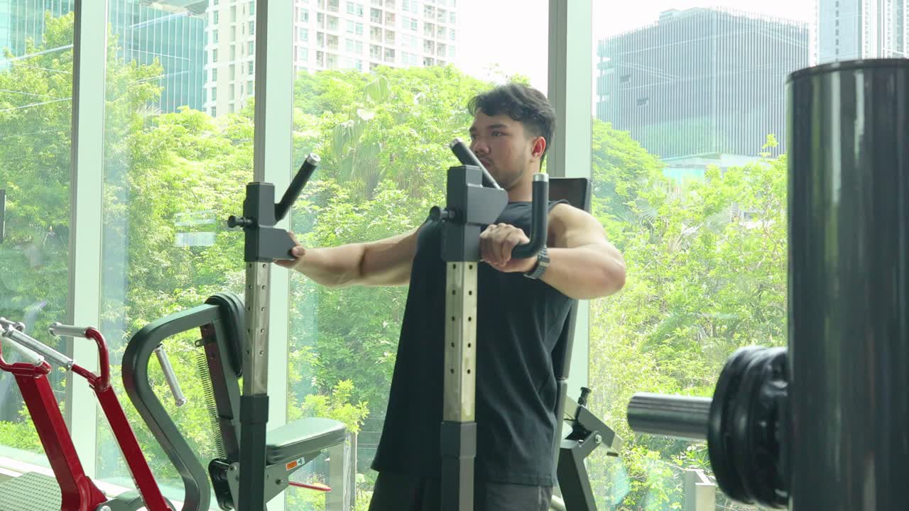 A man performs strength training on a gym machine in a well-lit room with a cityscape backdrop