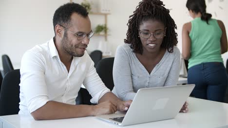 smiling colleagues talking and reading information from laptop