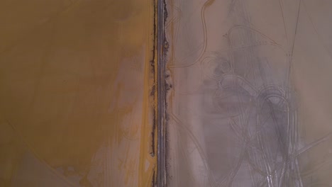 Disparo-De-Un-Dron-Volando-Sobre-Un-Camino-De-Tierra-Que-Se-Eleva-Para-Revelar-El-Lago-Salado-De-Salinas-Grandes-En-La-Frontera-De-Salta-Y-Jujuy,-Argentina.