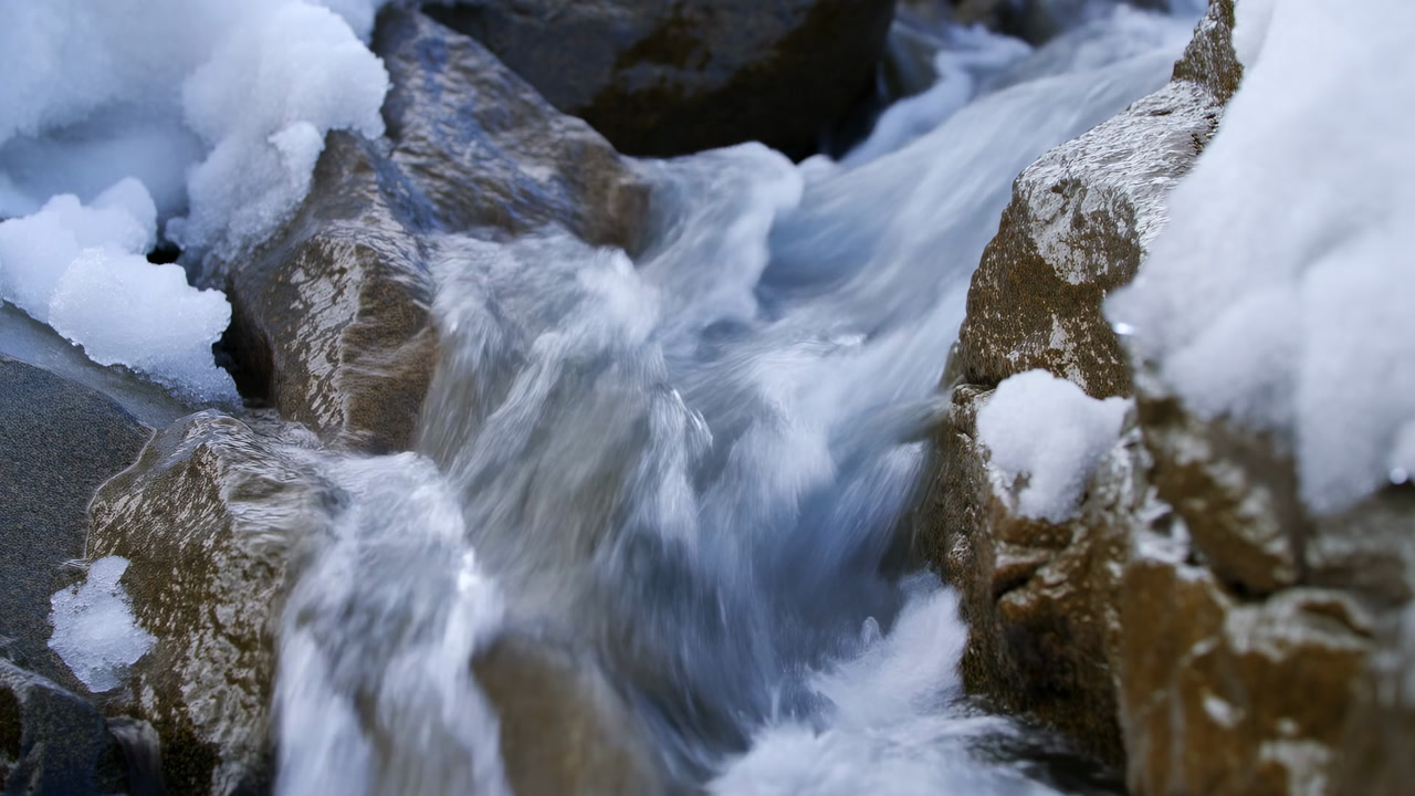 Snowy Mountain Stream Rushing Between Rocks, Cinematic Slow Motion Closeup Of Icy Water Melting Snow,