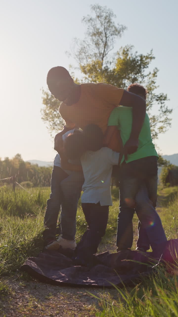 Papà sorridente che lotta e gioca con i suoi bambini all'aperto in una giornata di sole, godendosi il divertimento in famiglia