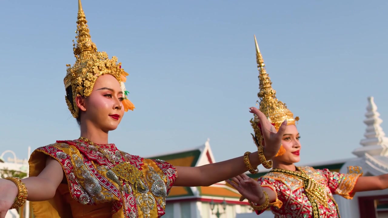Dos bailarines con elaborados trajes dorados realizan movimientos tradicionales de Khon a plena luz del día.