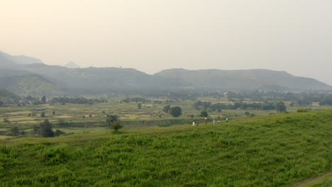 los lugareños caminando por una colina cubierta de hierba con vistas panorámicas a las montañas en karjat, maharashtra, india