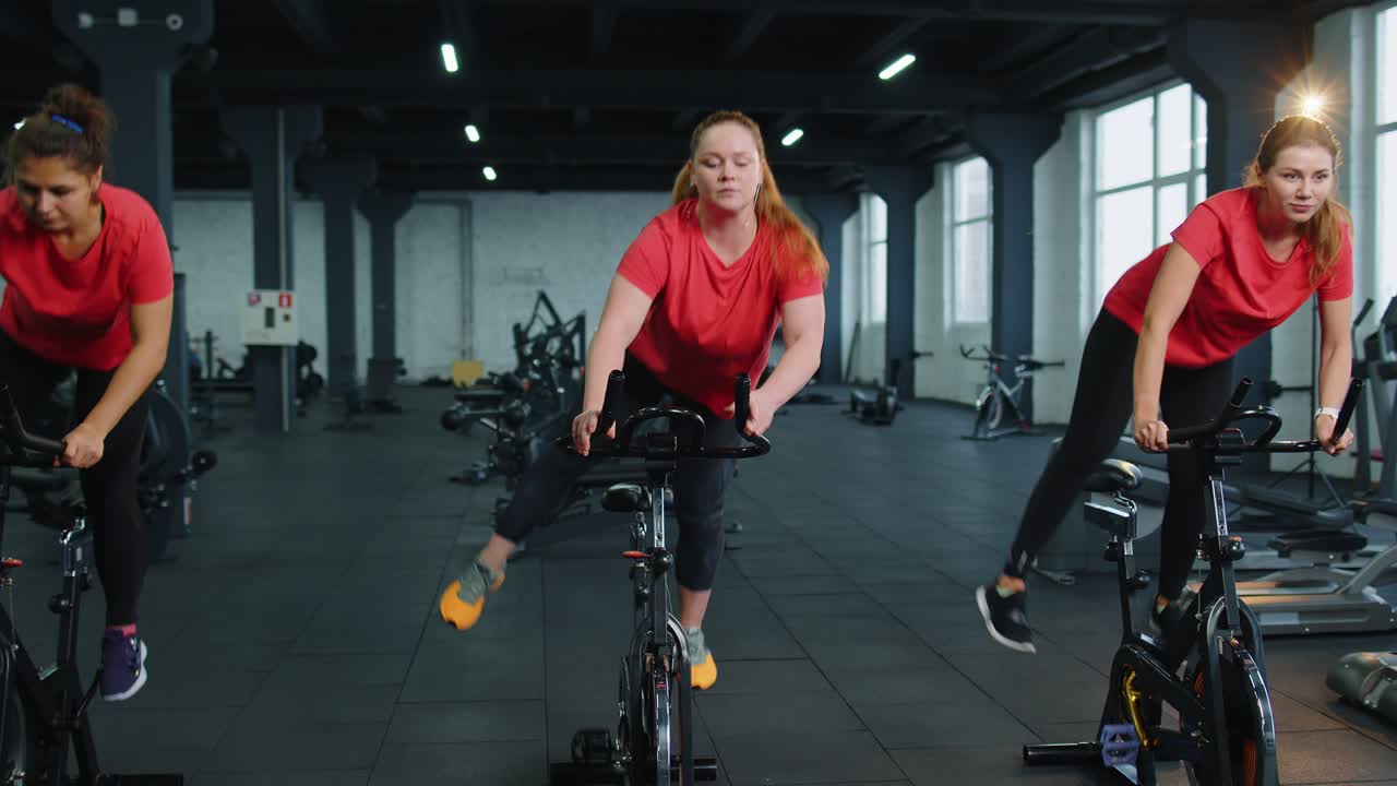 Gruppo di ragazze atletiche che eseguono esercizi di allenamento aerobico su cyclette in palestra.