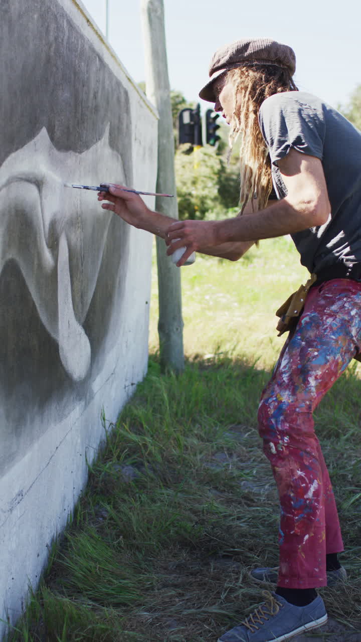 Video verticale di un artista maschio hipster caucasico con i capelli lunghi che dipinge un murale di balena su una parete.