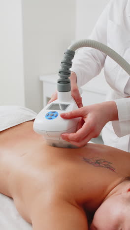 doctor makes woman cavitation lpg vacuum roller massage on back correction figures in spa clinic