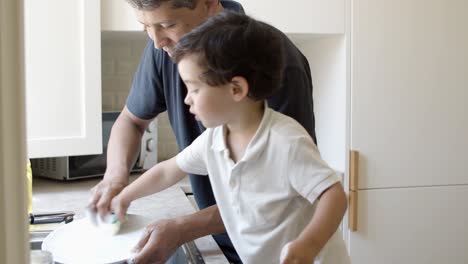 padre enseñando a su hijo pequeño a lavar platos