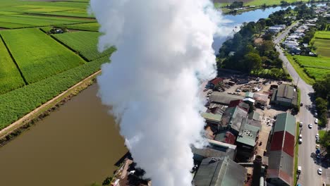 drone footage captures steam rising from a factory amidst lush fields, highlighting industrial impact on the environment