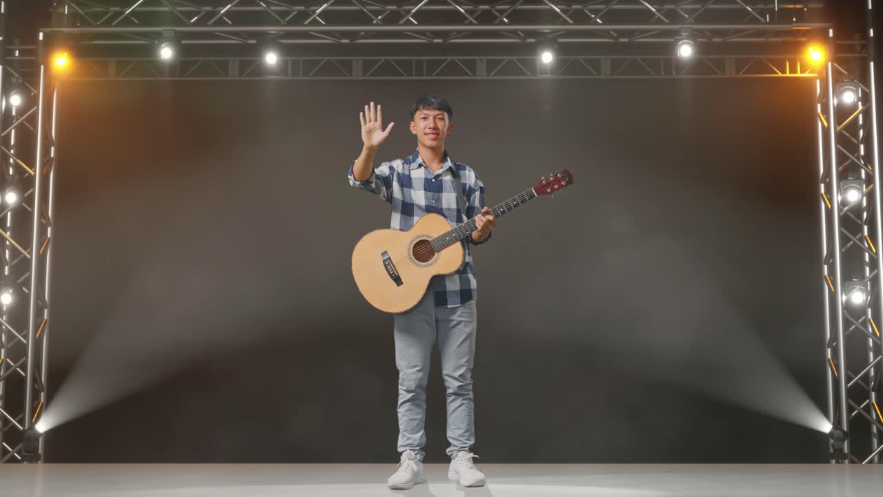 기타를 흔들고 무대에서 카메라에 미소 짓는 아시아 십대