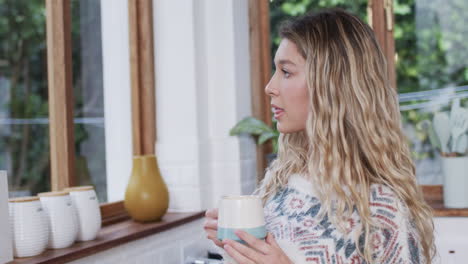 Portrait-of-happy-biracial-woman-with-blonde-hair-drinking-coffee-at-home,-copy-space,-slow-motion