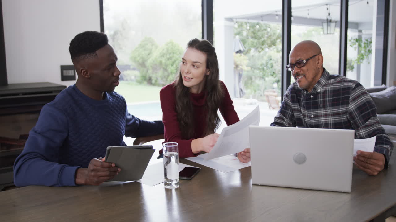 Happy diverse couple and financial advisor using laptop,tablet and documents at home,slow motion