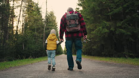 little boy and his granddad are walking to fishing in morning strolling on picturesque road in coniferous forest