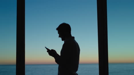 joven usando un teléfono inteligente en una habitación de hotel enviando mensajes de texto compartiendo el estilo de vida de vacaciones en las redes sociales disfrutando de la vista del océano al atardecer