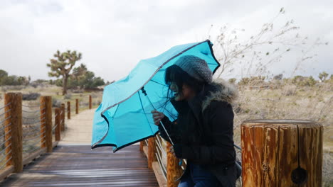 Una-Mujer-Joven-Y-Bonita-Sonriendo-Con-Mal-Tiempo-Con-Un-Paraguas-Azul-Durante-Una-Tormenta-Con-Viento-Fuerte