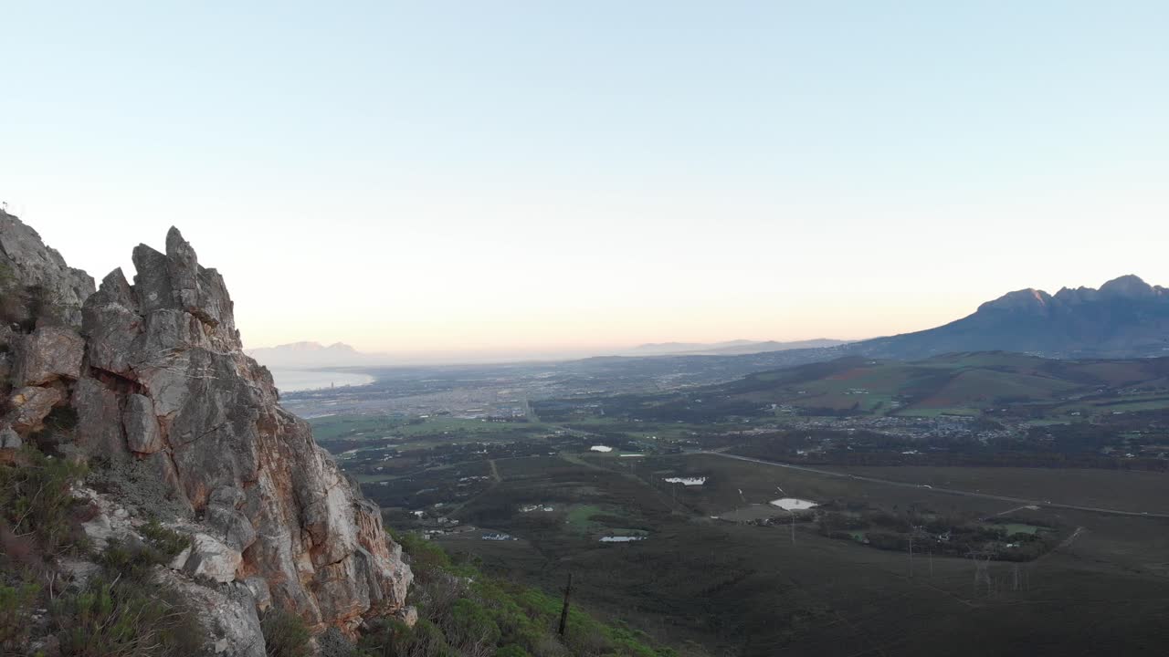 una toma de un dron que se mueve a lo largo de la ladera de una montaña y revela una vista nebulosa de la playa a lo lejos al atardecer