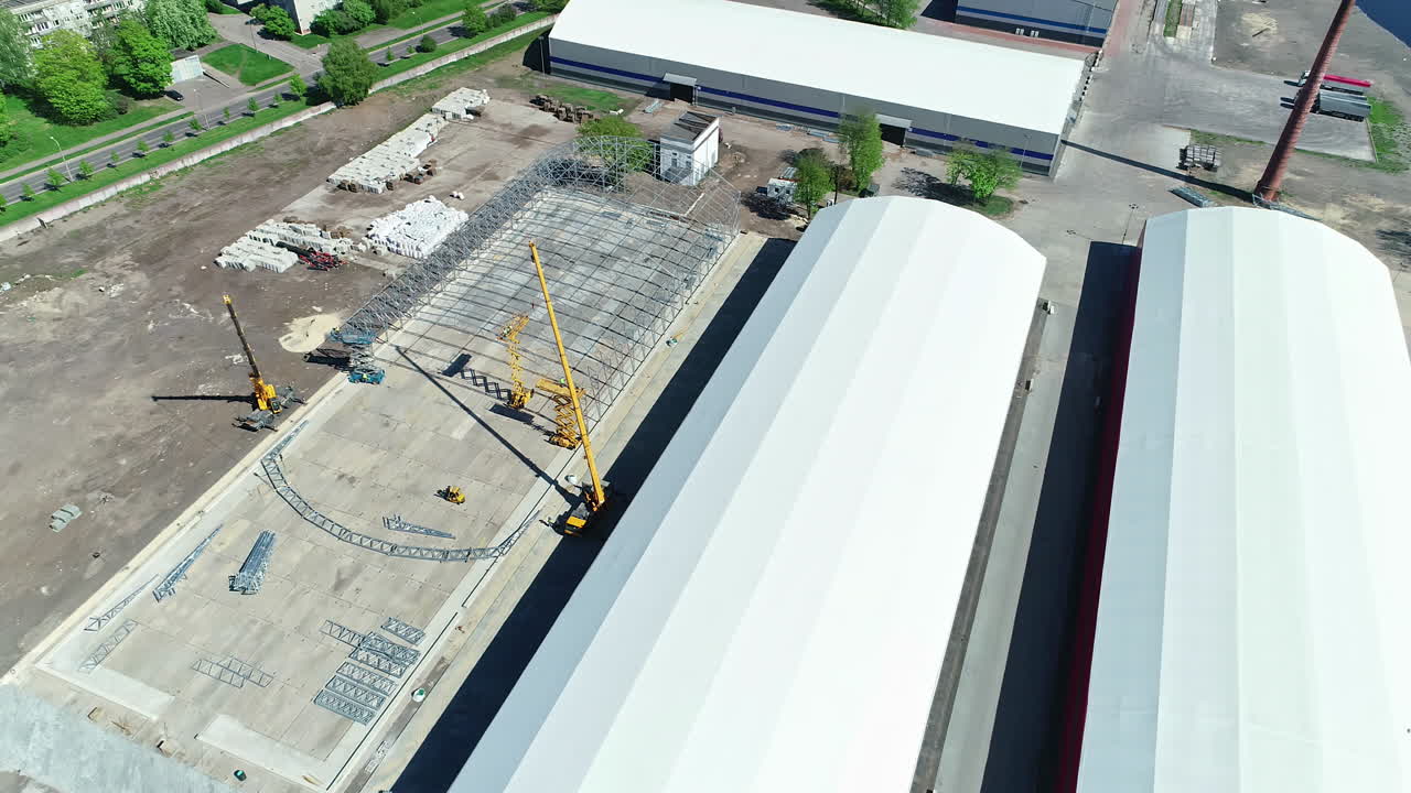 Aerial view of the construction site during construction works of a grain warehouse with cranes and marked foundation from bird's eye view