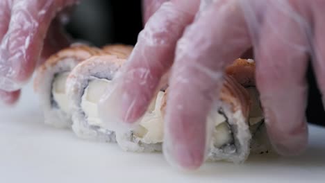 cook hands twist ready-made rolls of fish and rice on a white board