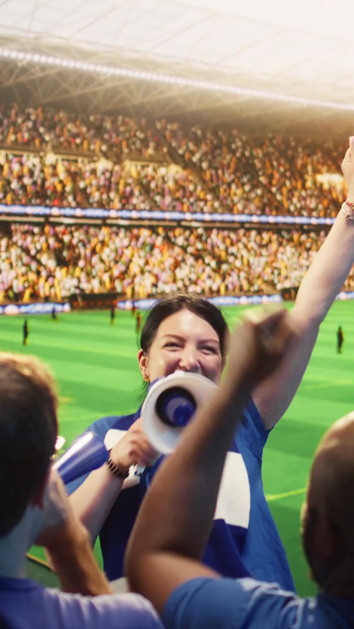 Video vertical: Mujer enérgica grita por megáfono en un estadio, liderando a los aficionados al fútbol.