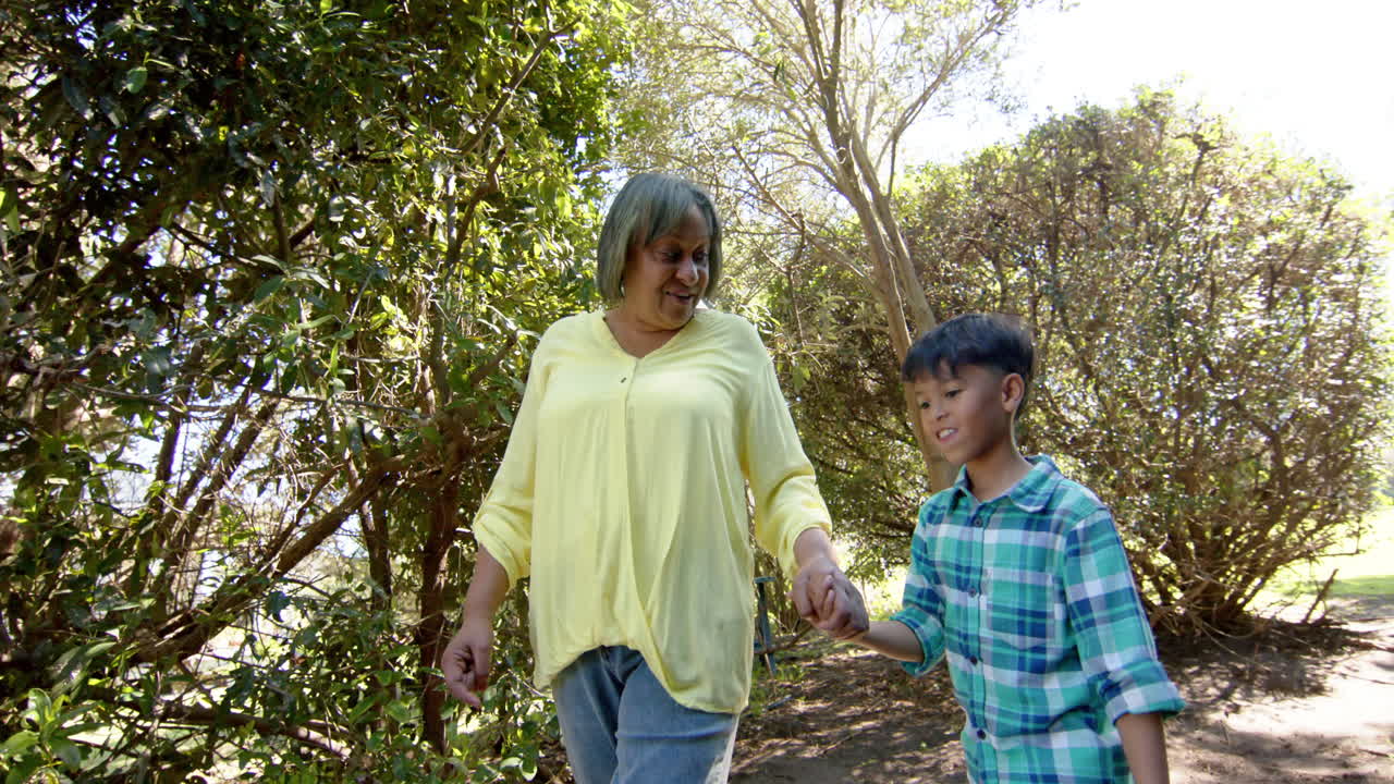 una abuela y un nieto bi-racial felices caminando en un jardín soleado, en cámara lenta