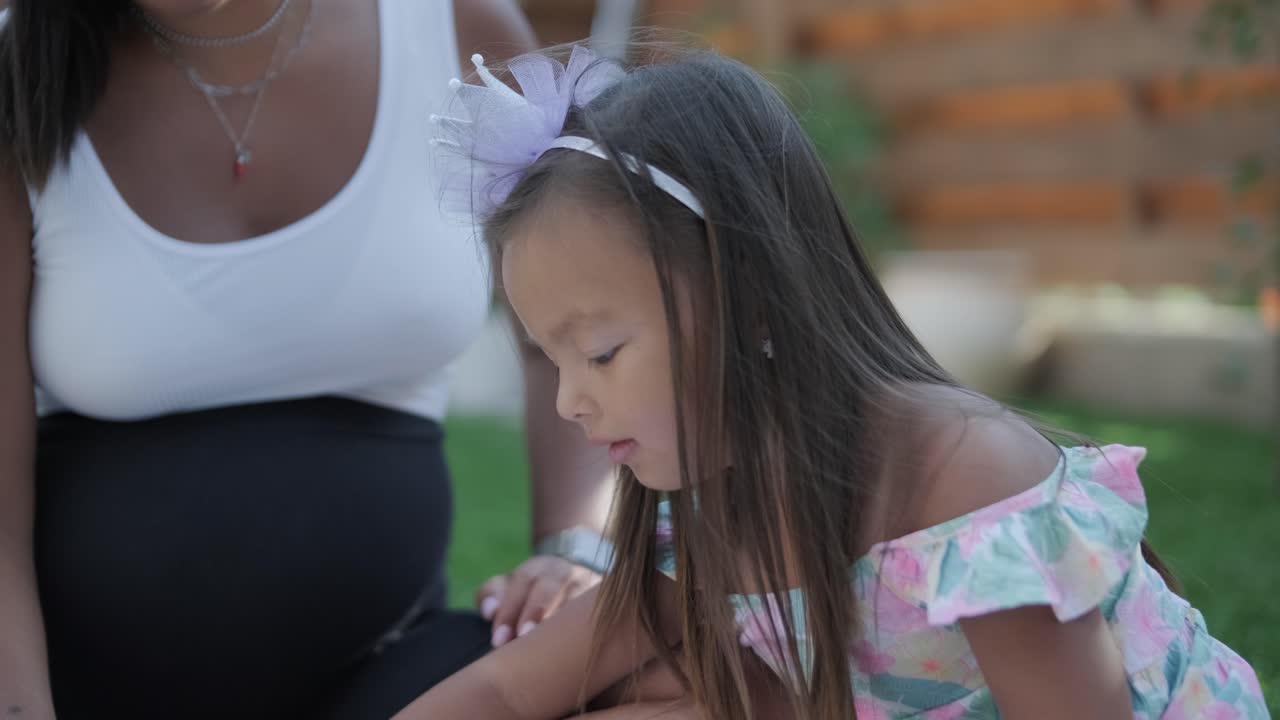 엄마와 어린 딸이 뒷마당에서 담요 위에 앉아 함께 그림을 그리고 있습니다. 야외 장면은 평화로운 가족 순간을 포착하여 창의성과 유대를 촉진합니다.