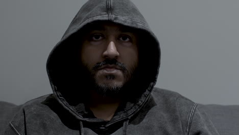 close up dolly shot of the face of an indian man wearing a hoodie, his eyes fixed in an intense determined stare while remaining completely motionless