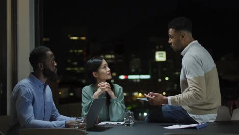 Video-of-biracial-businessman-talking-to-two-diverse-colleagues-at-night-in-office-meeting