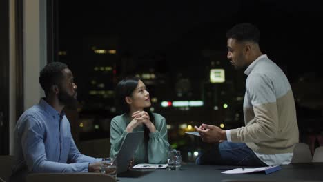 video of biracial businessman talking to two diverse colleagues at night in office meeting