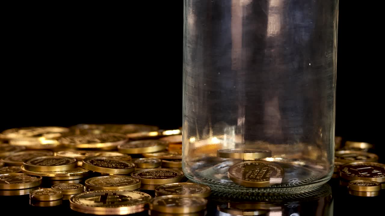 Multiple gold cryptocurrency tokens fall into a transparent jar, surrounded by coins, under studio lighting