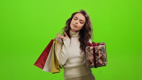 la mujer está sosteniendo un regalo y bolsas de compras. está pensando en algo. está de pie sobre un fondo verde. pantalla verde. 4k.