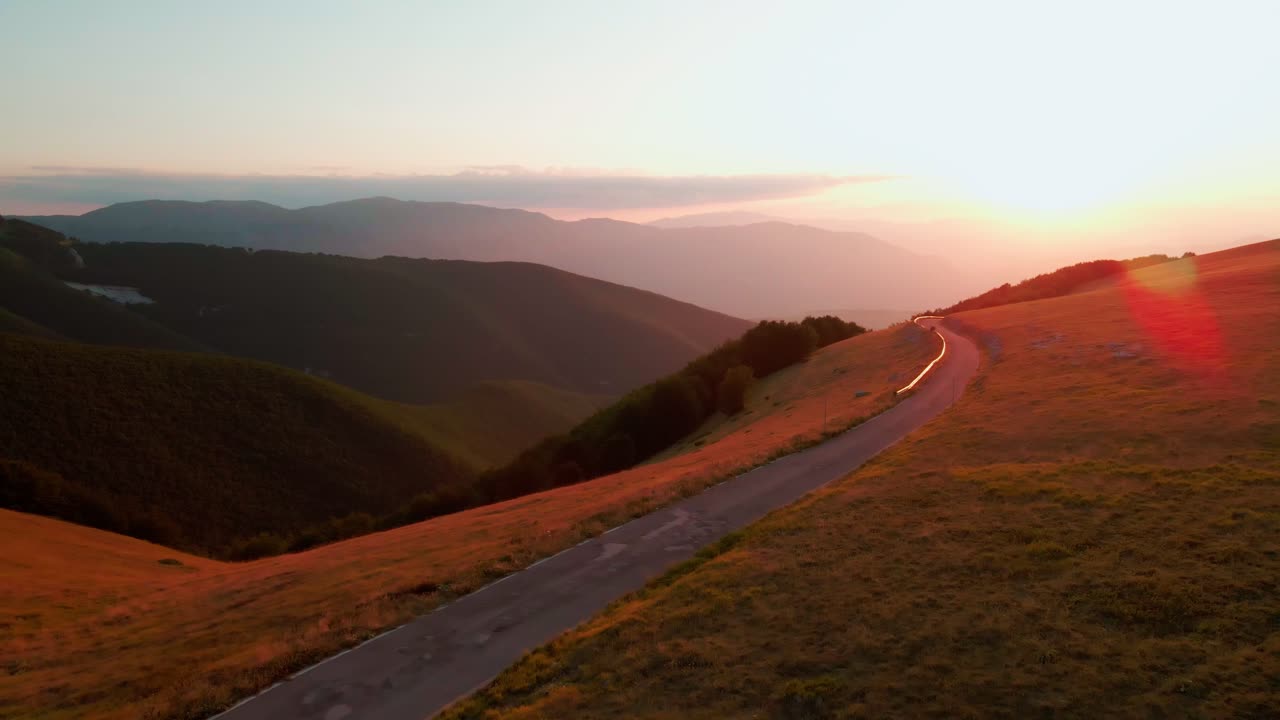 Scenic Sunset In The Majelletta Mountains, Abruzzo, Italy, a white van parked on the lawn near the road - aerial drone shot