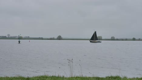 sailboat with a black sail sailing through the strait on a rainy, windy day with gray clouds