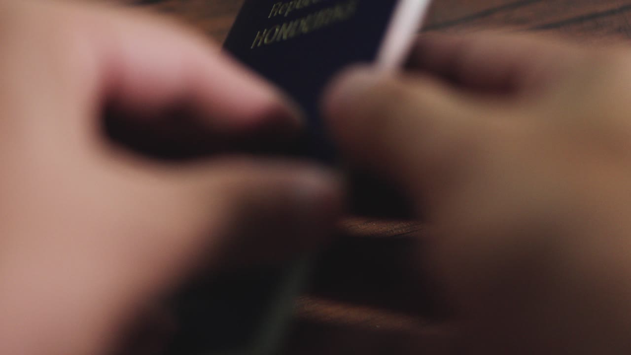 POV of a traveler flipping through the Honduran passport and placing it on the wooden table