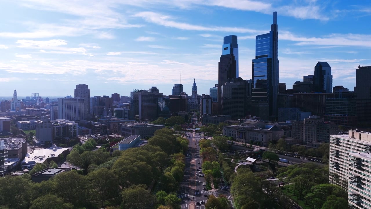 Vista aerea con drone della Benjamin Franklin Parkway di Filadelfia con Logan Circle, fiancheggiata da moderni grattacieli di vetro, la torre del Municipio e un cielo azzurro limpido.