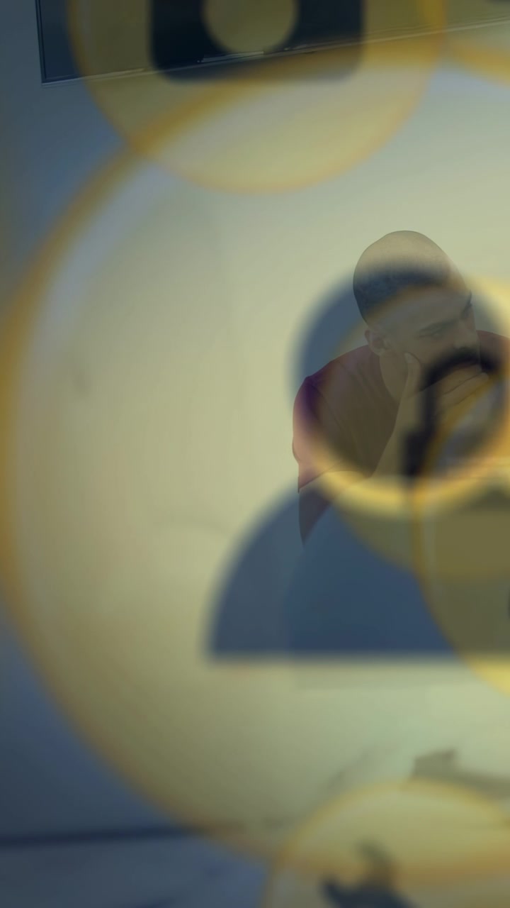 Vertical video: Seated man touching face while gold profile rings sweeping onto frame, showing tech