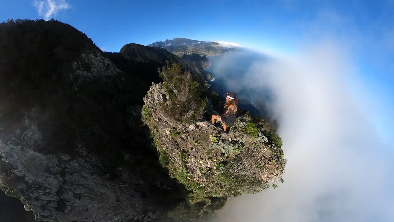 젊고 건강하고 강한 남자가 맑고 푸른 하늘과 함께 덥고 화창한 여름날 마데리아의 에스피가오 아모렐로 산 가장자리에 360개의 카메라가 달린 셀카봉을 들고 혼자 등반하고 달리고 있습니다.