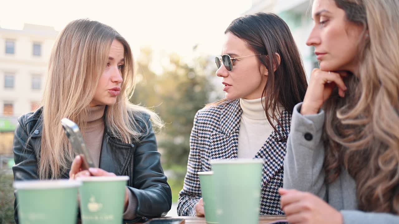 Three women talking and drinking coffee at a terrace
