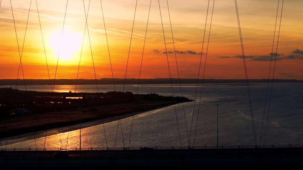 침착한 장면이 펼쳐집니다. 해가 지는 동안 바지 보트가 험버 다리  ⁇ 에서 조용히 미끄러지면서, 반 ⁇ 이는 강에 따뜻하고 황금색의 색조를 끼치고, 숨가 ⁇ 는 항공 영상으로 포착됩니다.