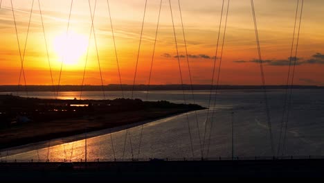 una escena tranquila se desarrolla como un barco de barcaza se desliza serenamente bajo el puente humber durante la puesta del sol, proyectando un tono cálido y dorado sobre el río reluciente, capturado en impresionantes imágenes aéreas