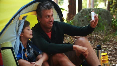 father and son taking a selfie on mobile phone outside tent