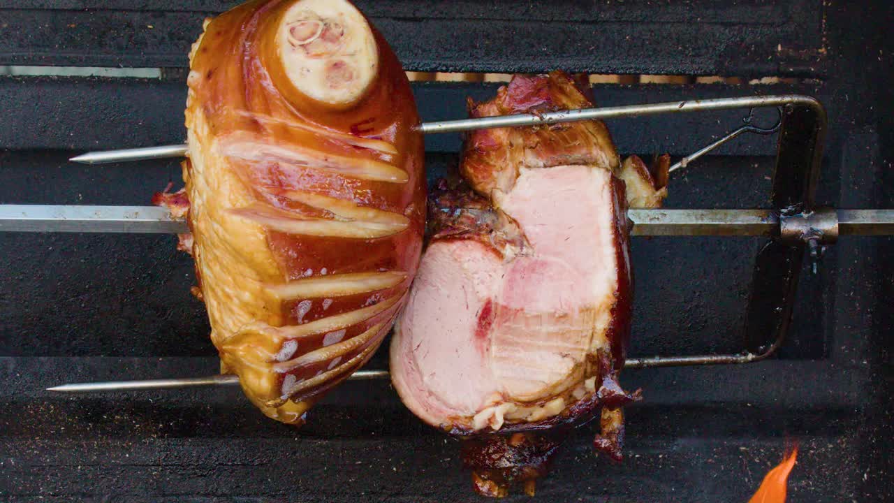 Juicy pork knuckle slowly rotates on a spit above open flames, traditional street food preparation