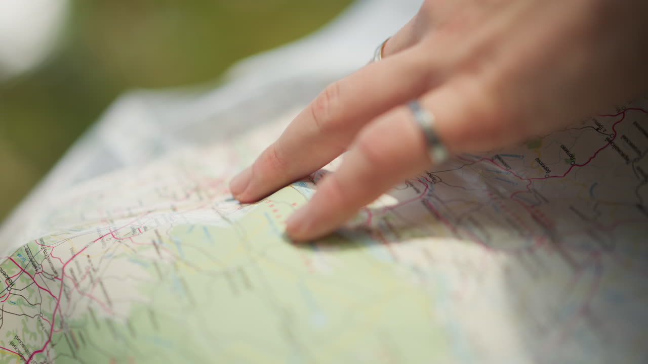 Hender peker på kartdestinasjon, solfylt utendørs engbakgrunn, sølvringer, fingertupp trykker på rute, reiseblogger planlegger biltur, ivrig forventning, lav dybdeskarphet