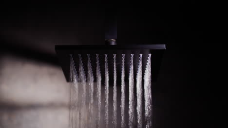 toma cinematográfica: el agua fluye de una boquilla cuadrada negra en la ducha.