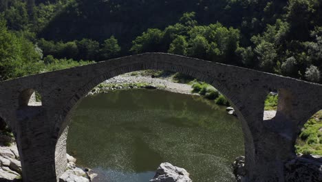 retreating drone shot revealing the full length of the devil's bridge situated in ardino at the foot of rhodope mountain in bulgaria