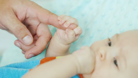 Baby,-Das-Den-Finger-Seines-Vaters-Hält,-Nagt-An-Seiner-Faust-Konzeptunterstützung-Und-Pflege-Der-Eltern