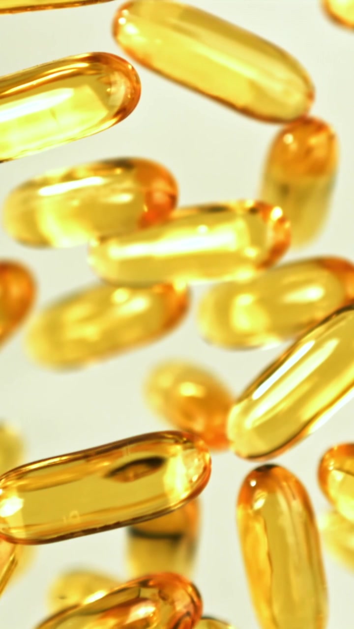 Capsule softgel dorate di Omega 3 a fuoco su sfondo bianco