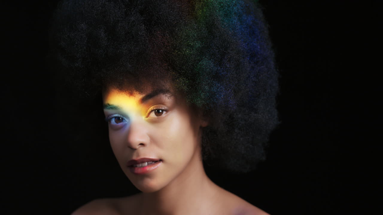 ritratto multicolore ravvicinato bella donna afroamericana con afro che gode di una pelle liscia e sana che sembra sicura bellezza naturale luce colorata su sfondo nero concetto di cura della pelle