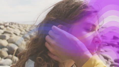 young woman adjusting hair with purple wave animation over rocky beach background