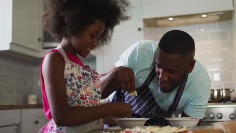 hija afroamericana y su padre haciendo pizza juntos en la cocina